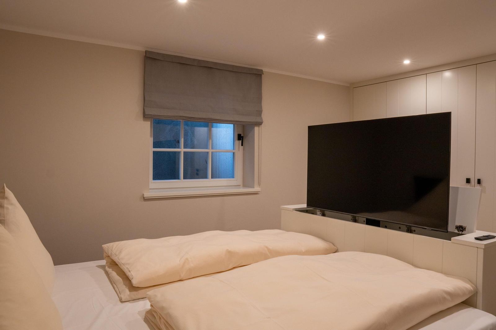 Schlafzimmer mit Bett, Fenster und Fernseher an der Wand.
