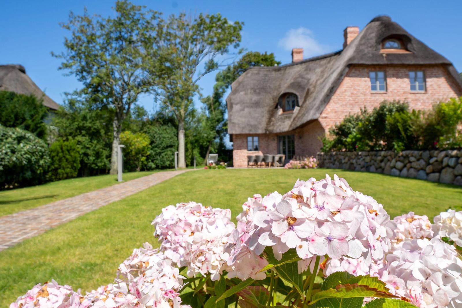 Haus mit Strohdach und Gartenweg mit Blumen im Vordergrund.
