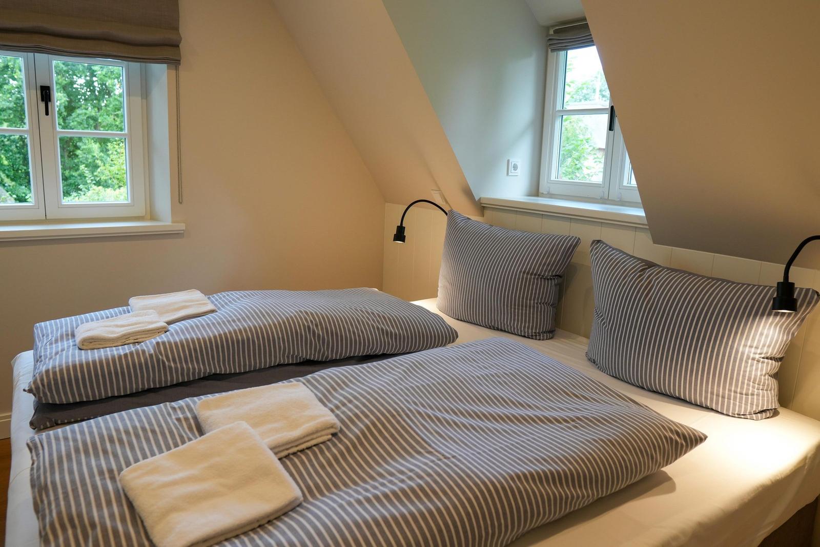 Schlafzimmer mit Doppelbett, zwei Fenstern und zwei Nachttischen mit Lampen.