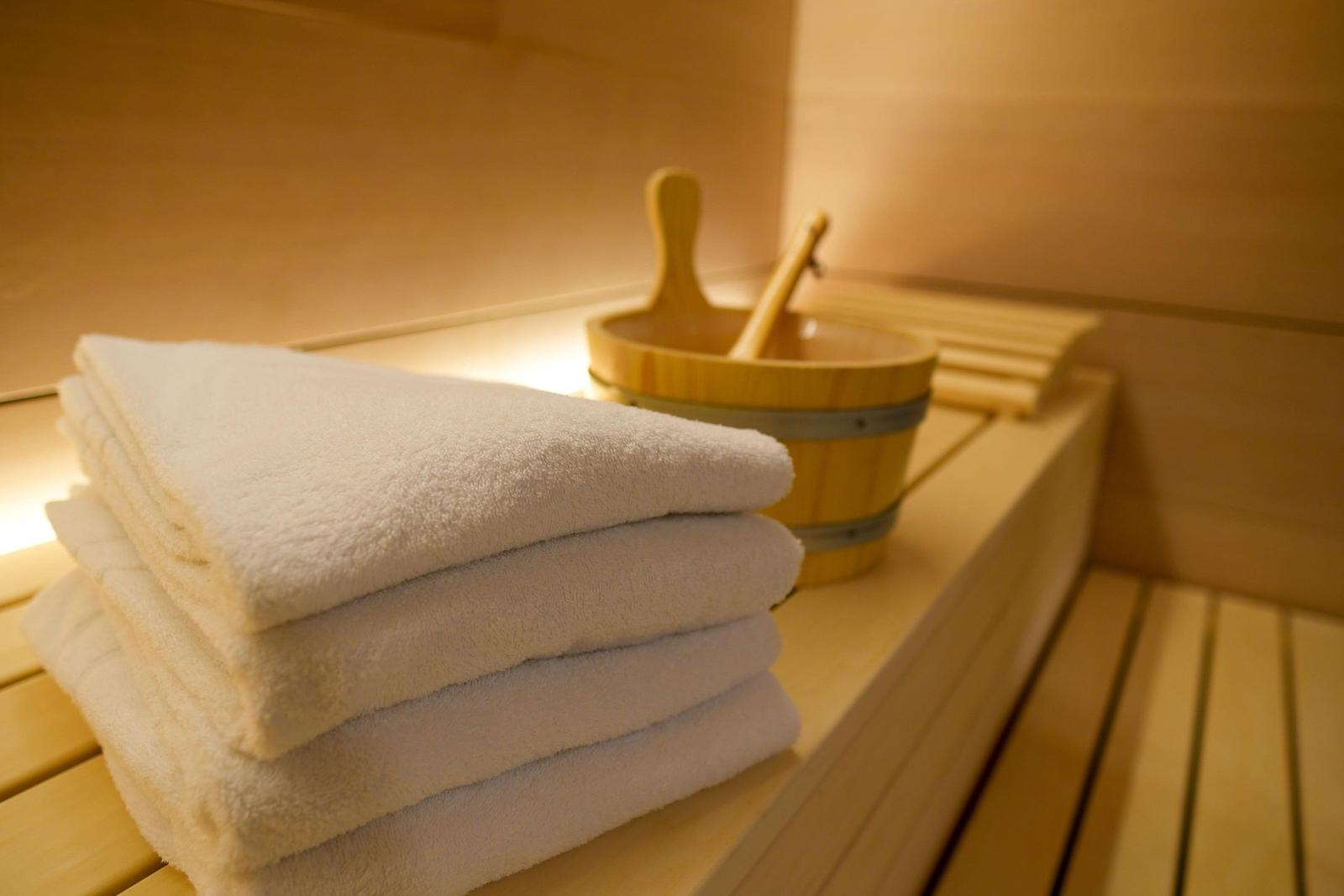 Sauna mit Holzbank, gefalteten weißen Handtüchern und Holzschale mit Löffeln.