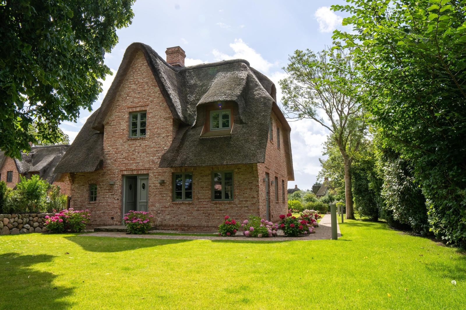 Haus mit strohgedecktem Dach und grünem Garten mit Blumenbeeten.