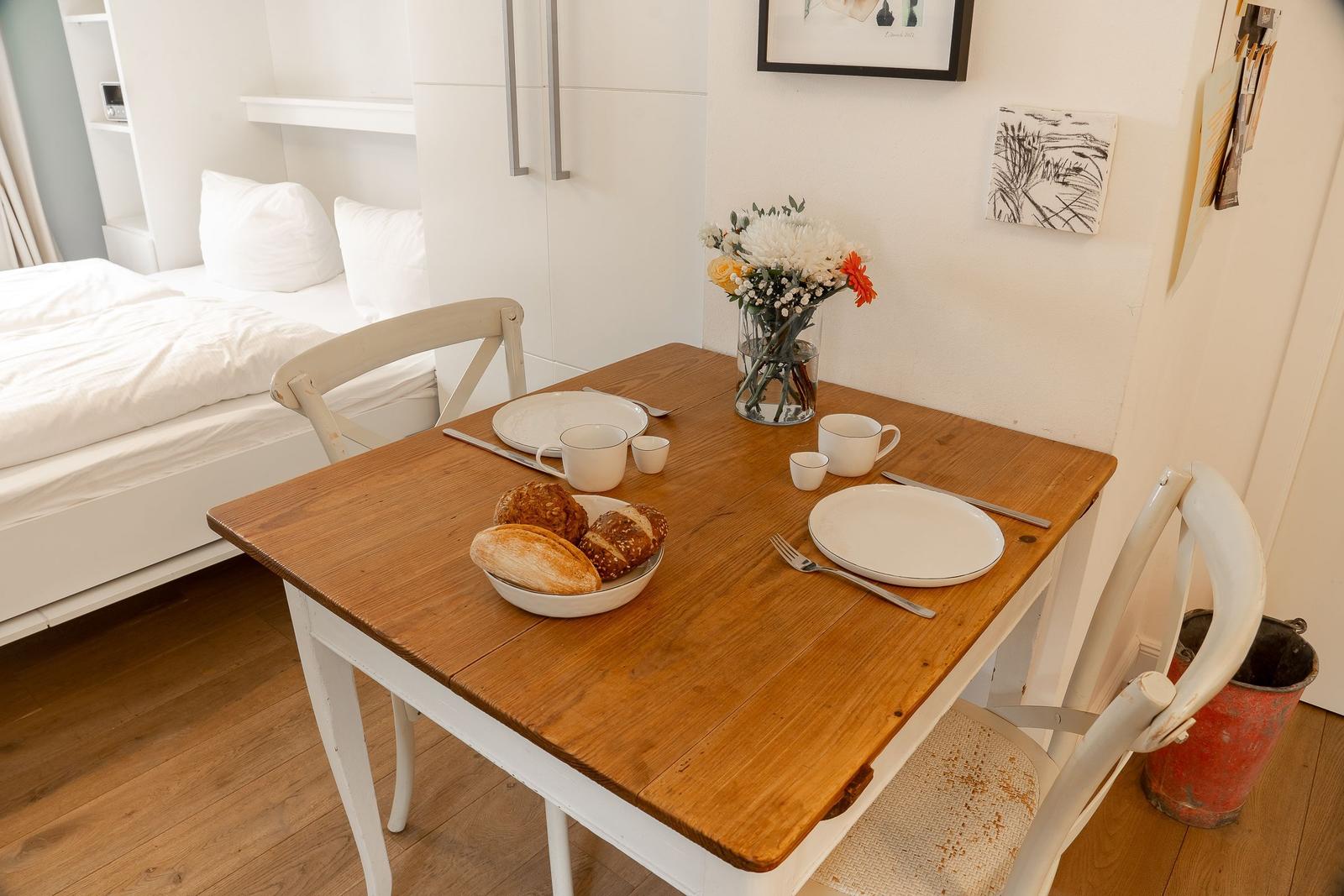 Holztisch mit Frühstück und Bett im Hintergrund.