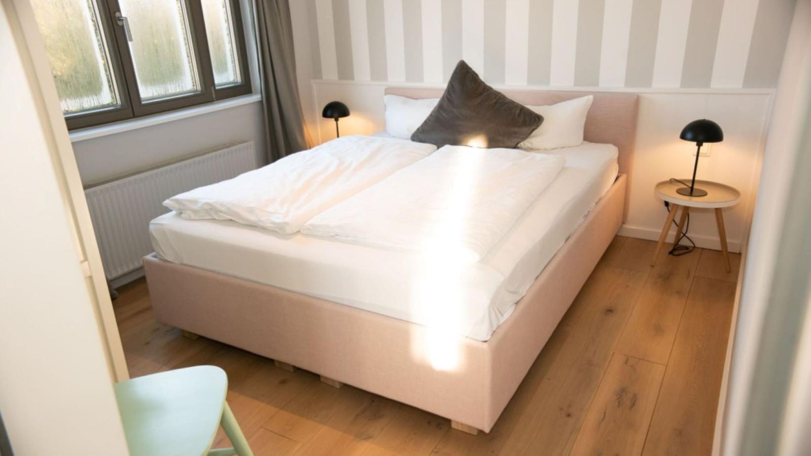 Schlafzimmer mit Bett, Nachttisch und Lampe. Holzboden und gestreifter Wandverkleidung.