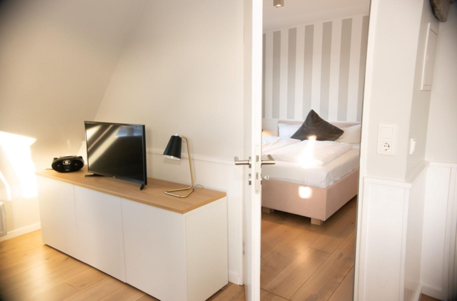 Schlafzimmer mit Bett und Streifenwand. Wohnbereich mit TV und Schrank.