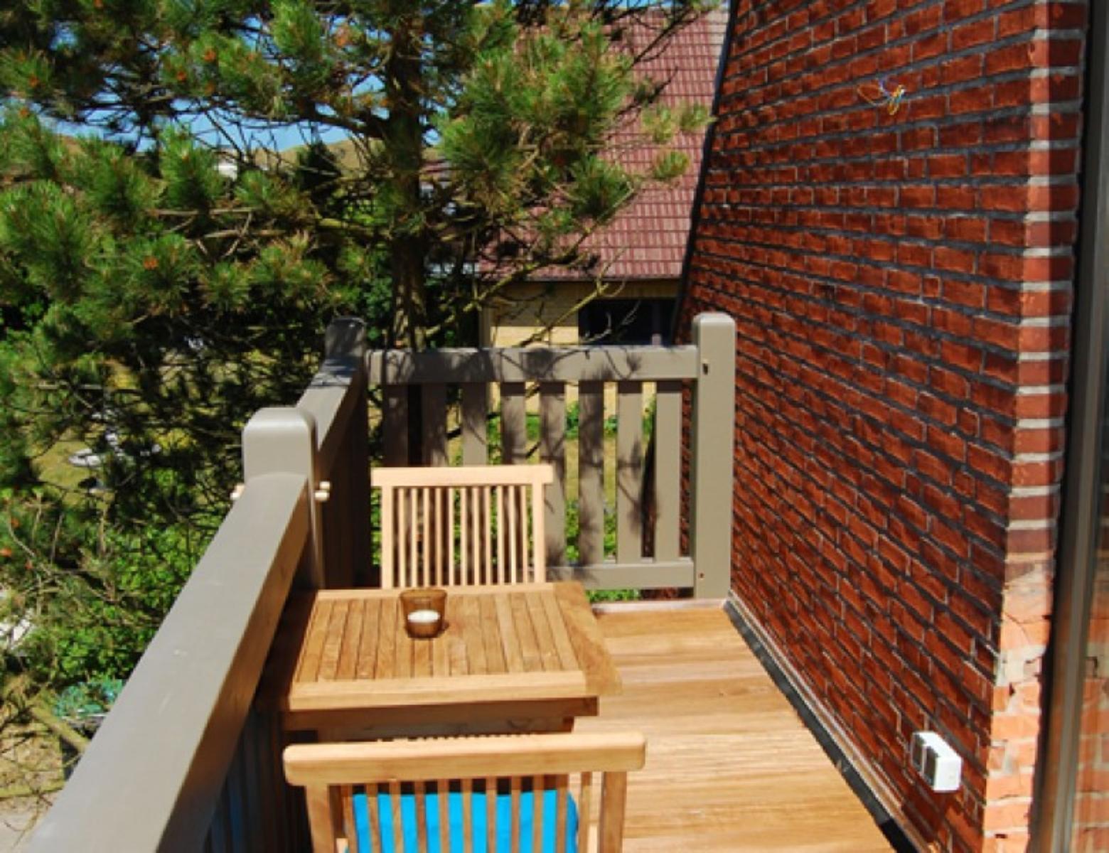 Terrasse mit Holztisch und Stühlen, roter Backsteinwand und grüner Umgebung.