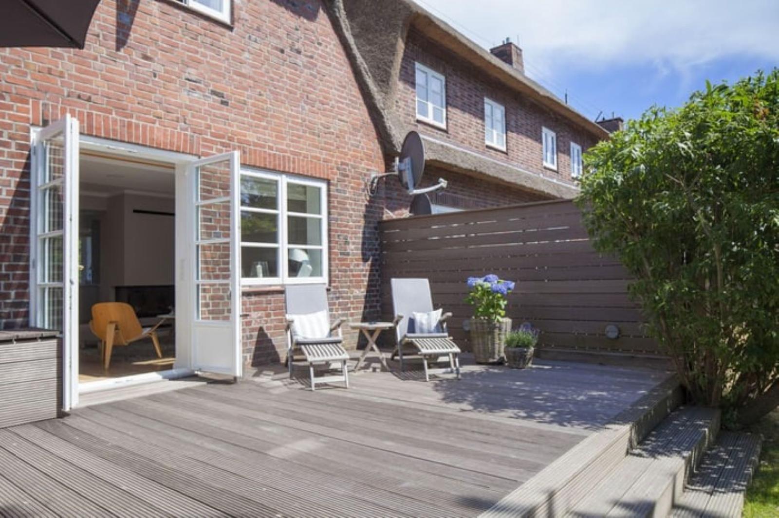 Terrasse mit Sitzgelegenheiten und Blick in das Haus. Holzdeck und Pflanzen sind sichtbar.