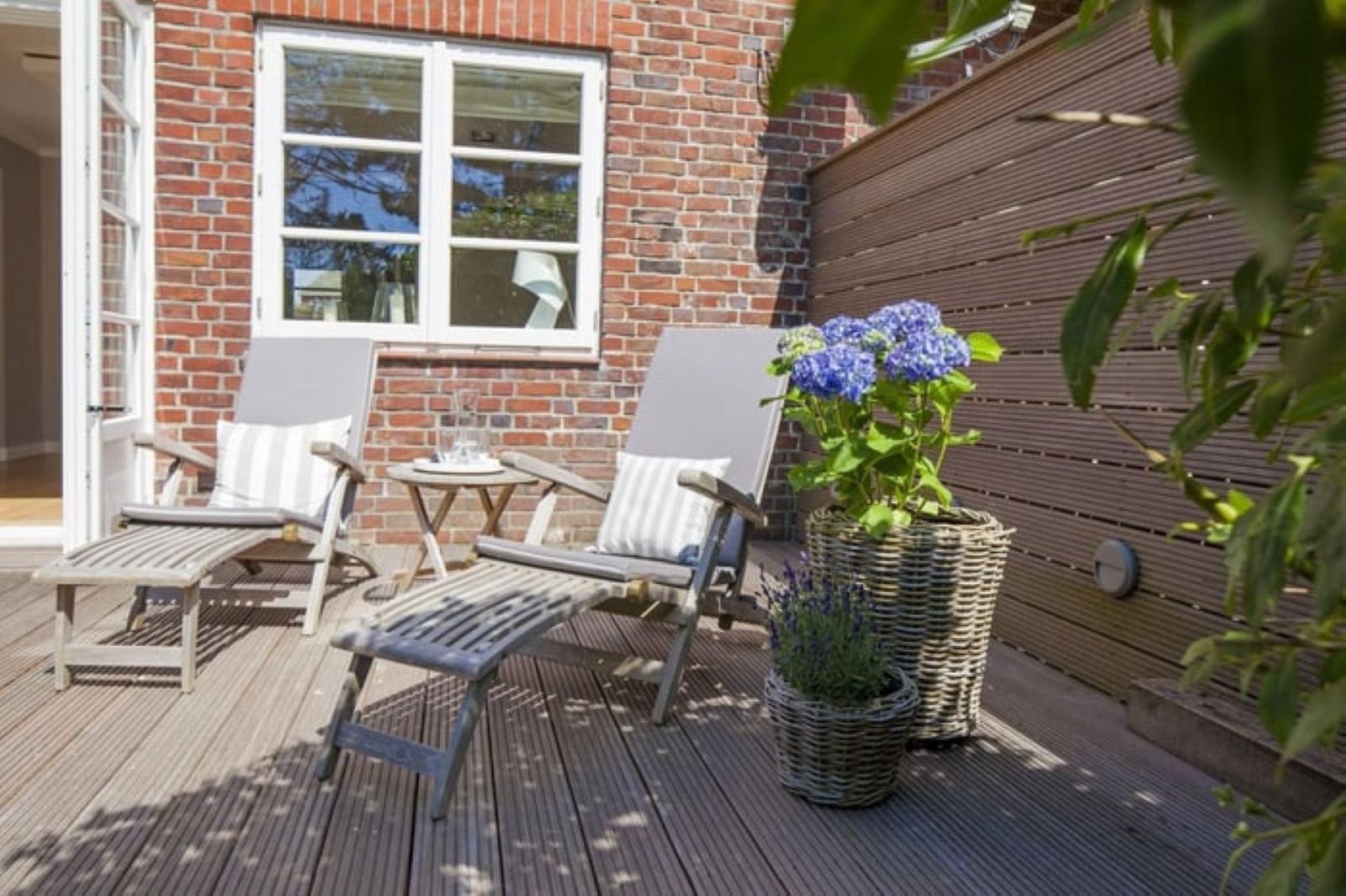 Terrasse mit zwei Liegestühlen, Tisch und Blumen in Körben.