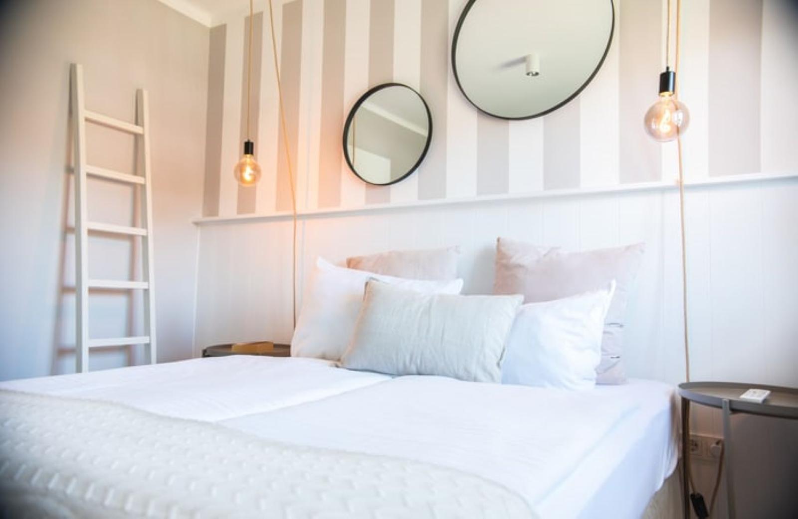 Schlafzimmer mit Bett, zwei runden Spiegeln und einer Leiter an der Wand.