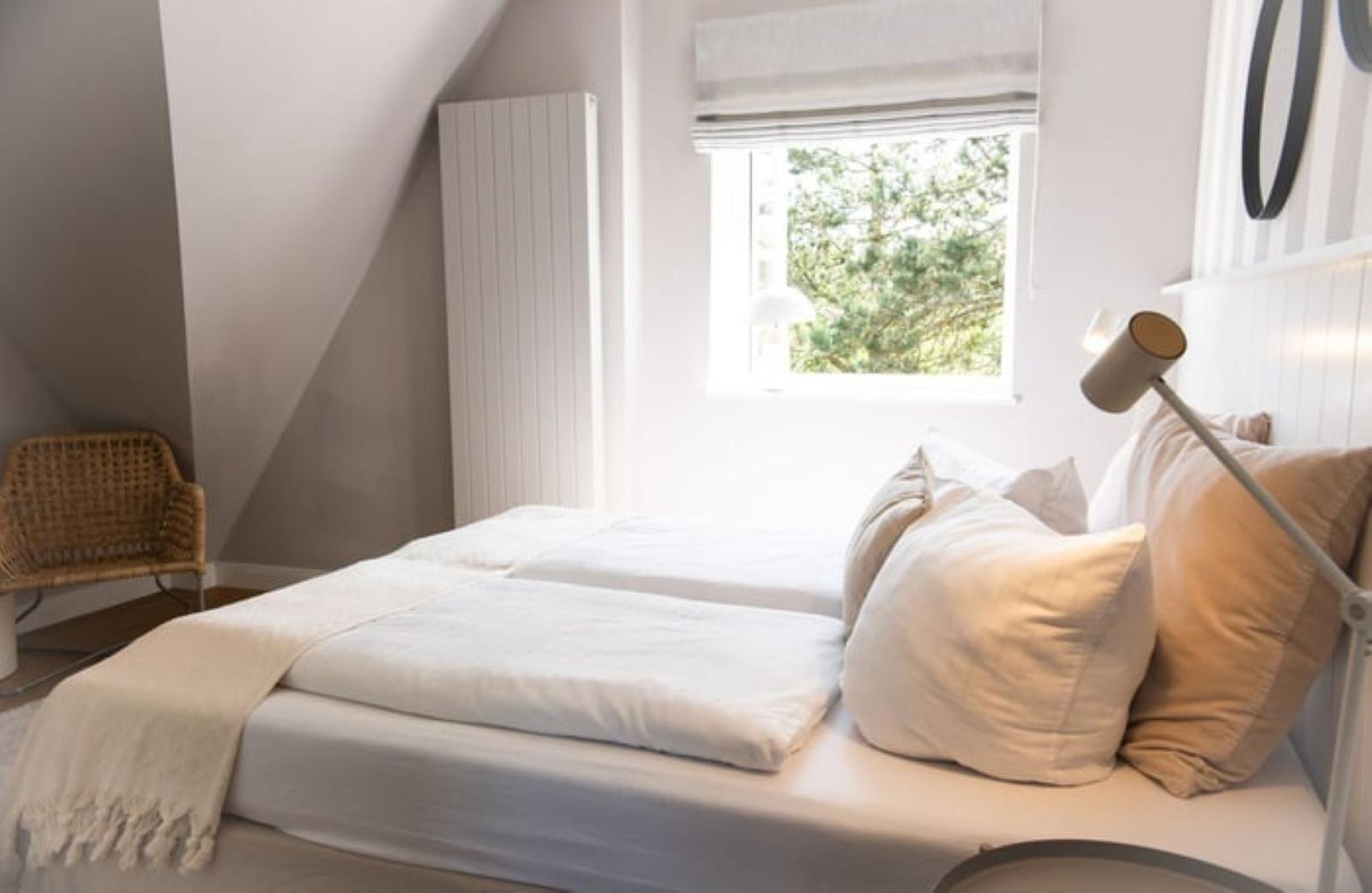 Schlafzimmer mit Dachschrägen, Bett, Fenster und Stuhl.