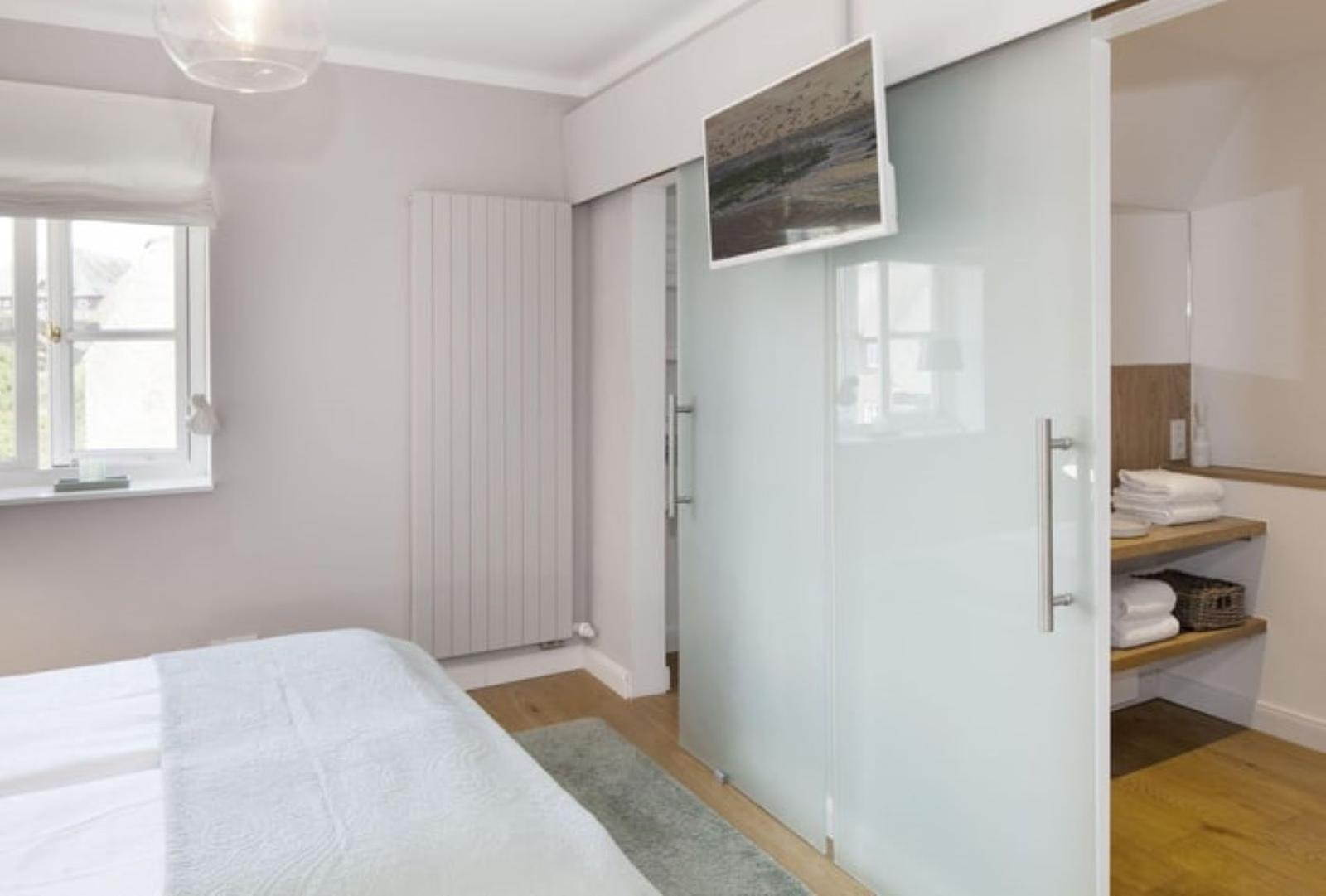 Schlafzimmer mit Bett, Fenster und Schlafzimmerwand. Fernseher an der Wand.