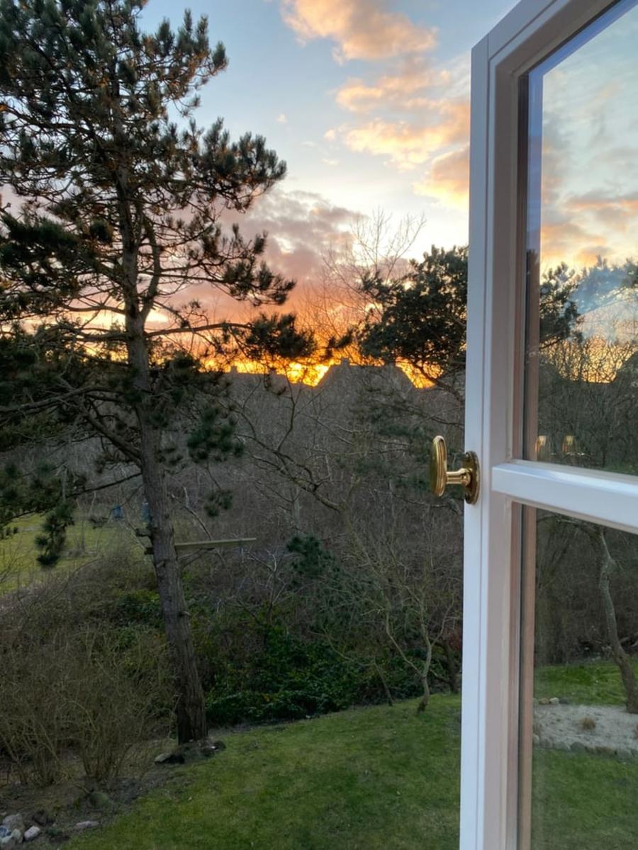 Durch das Fenster blickt man auf einen Garten mit Bäumen und einen Sonnenuntergang.