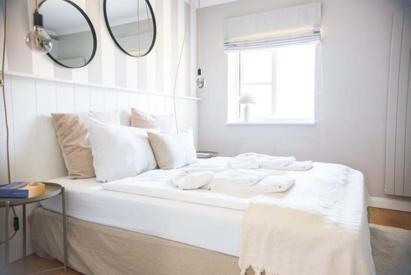 Schlafzimmer mit Bett, Kissen und Fenster. Zwei runde Spiegel an der Wand.