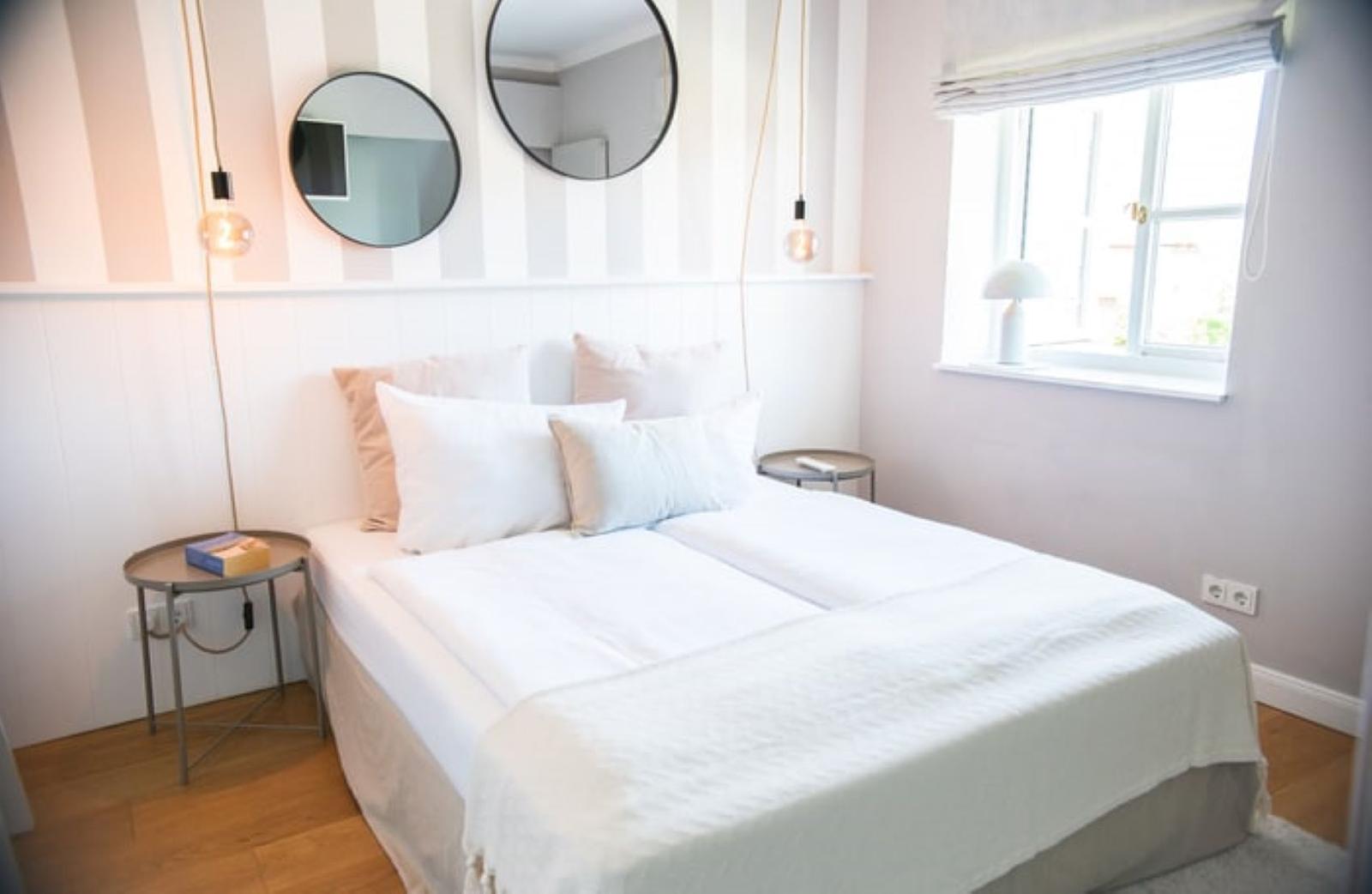 Schlafzimmer mit Bett, zwei runden Spiegeln und Fenster mit Lampen.