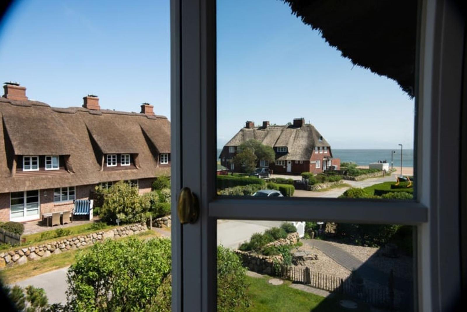 Ansicht durch Fenster auf Dachhäuser und Strand.