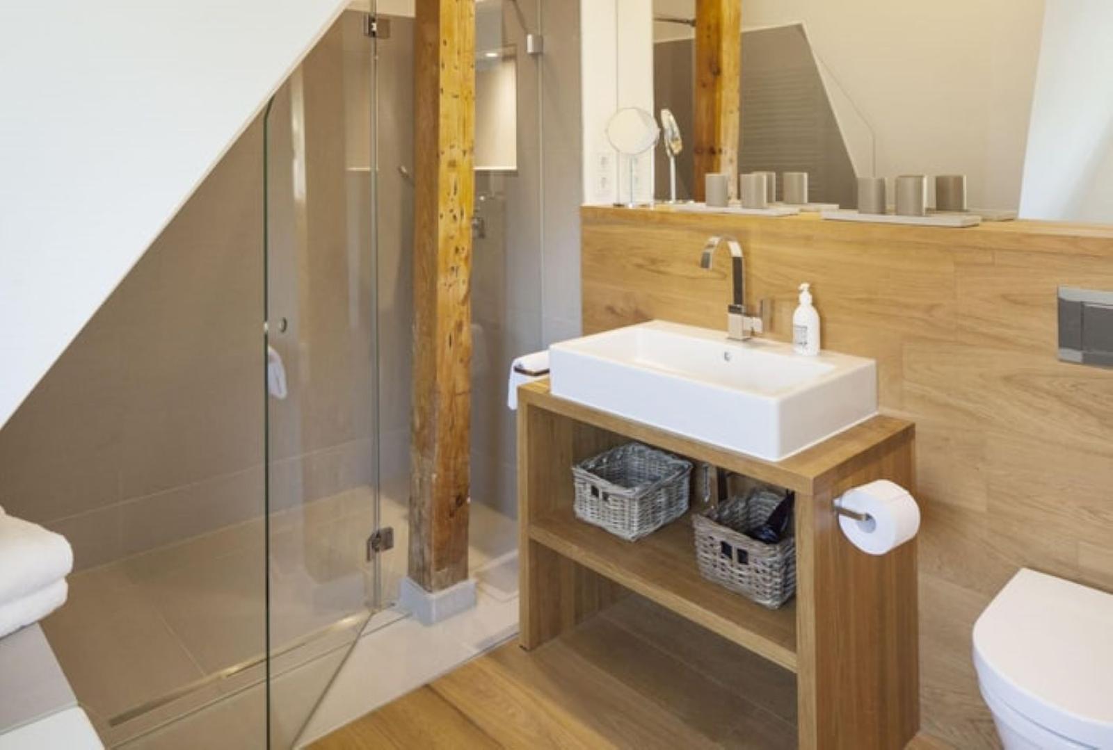 Badezimmer mit Dusche, Waschbecken und Toilette. Holz- und Glasgestaltung.