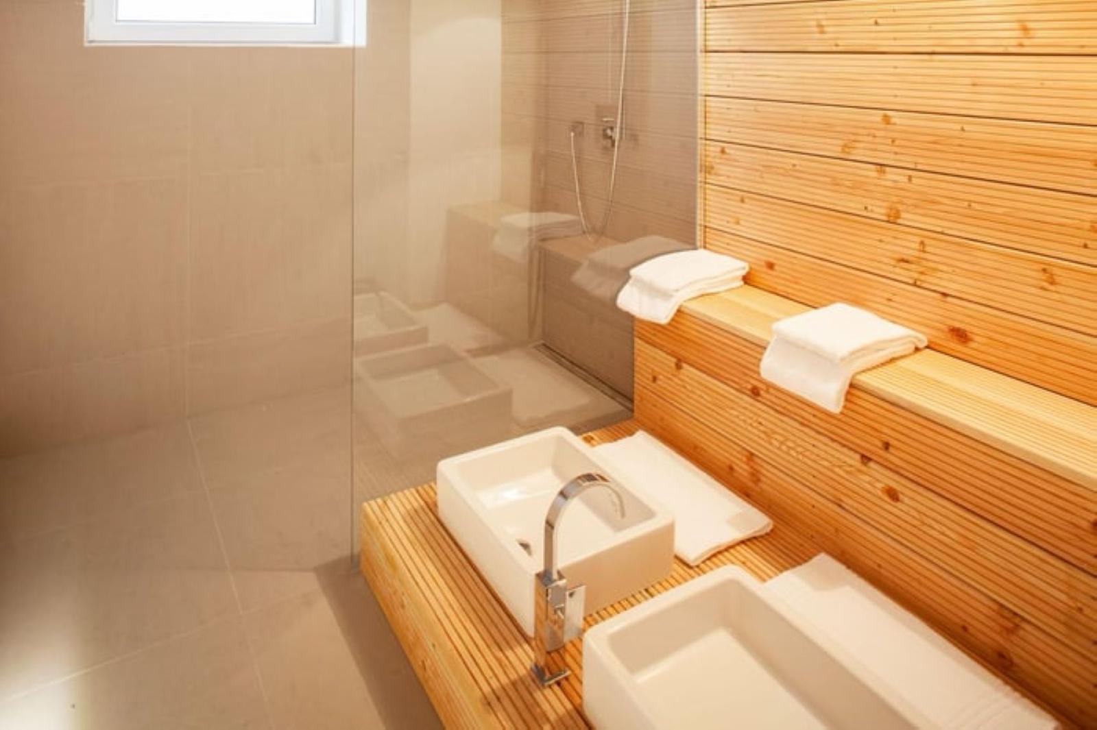Bad mit Dusche, zwei Waschbecken und Holzbank mit Handtüchern.