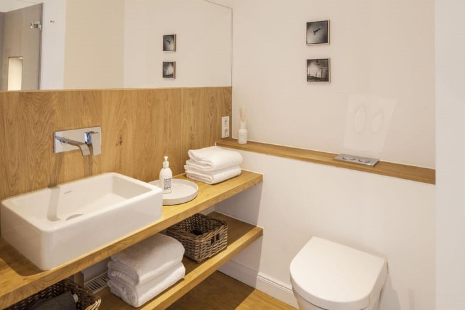 Badezimmer mit Waschbecken, Toilette und Holzregalen.
