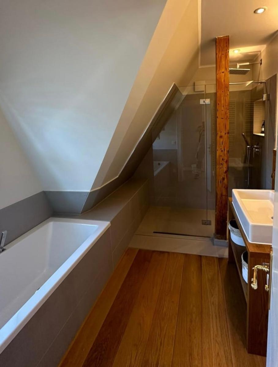 Dusche mit Glaswand, Badewanne und Holzboden in Dachschrägen
