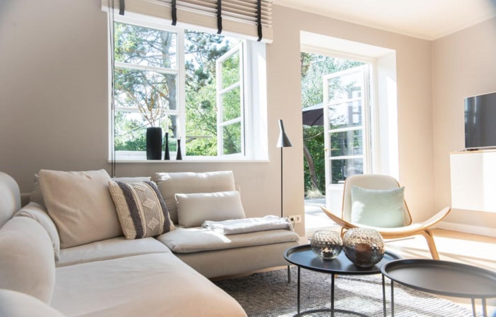 Wohnzimmer mit Sofa, Sessel und Tischen. Fenster und Tür zur Außenterrasse.
