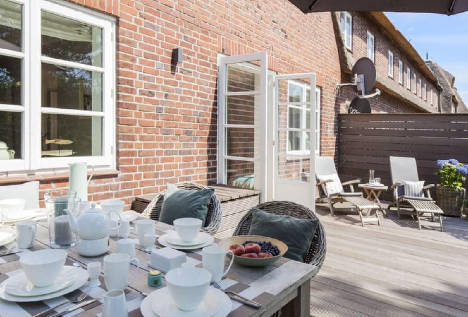 Terrasse mit gedecktem Tisch, Sitzgelegenheiten und Blick auf Backsteinhaus.