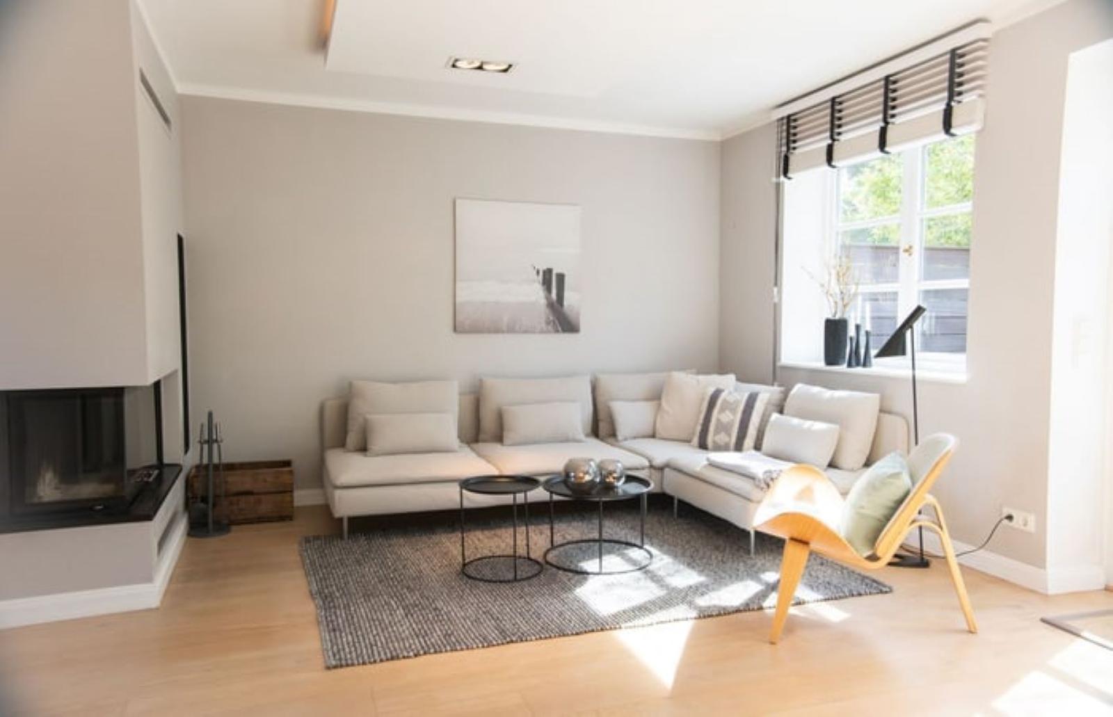 Wohnzimmer mit Ecksofa, Kamin und Holzboden. Fenster mit Jalousie.