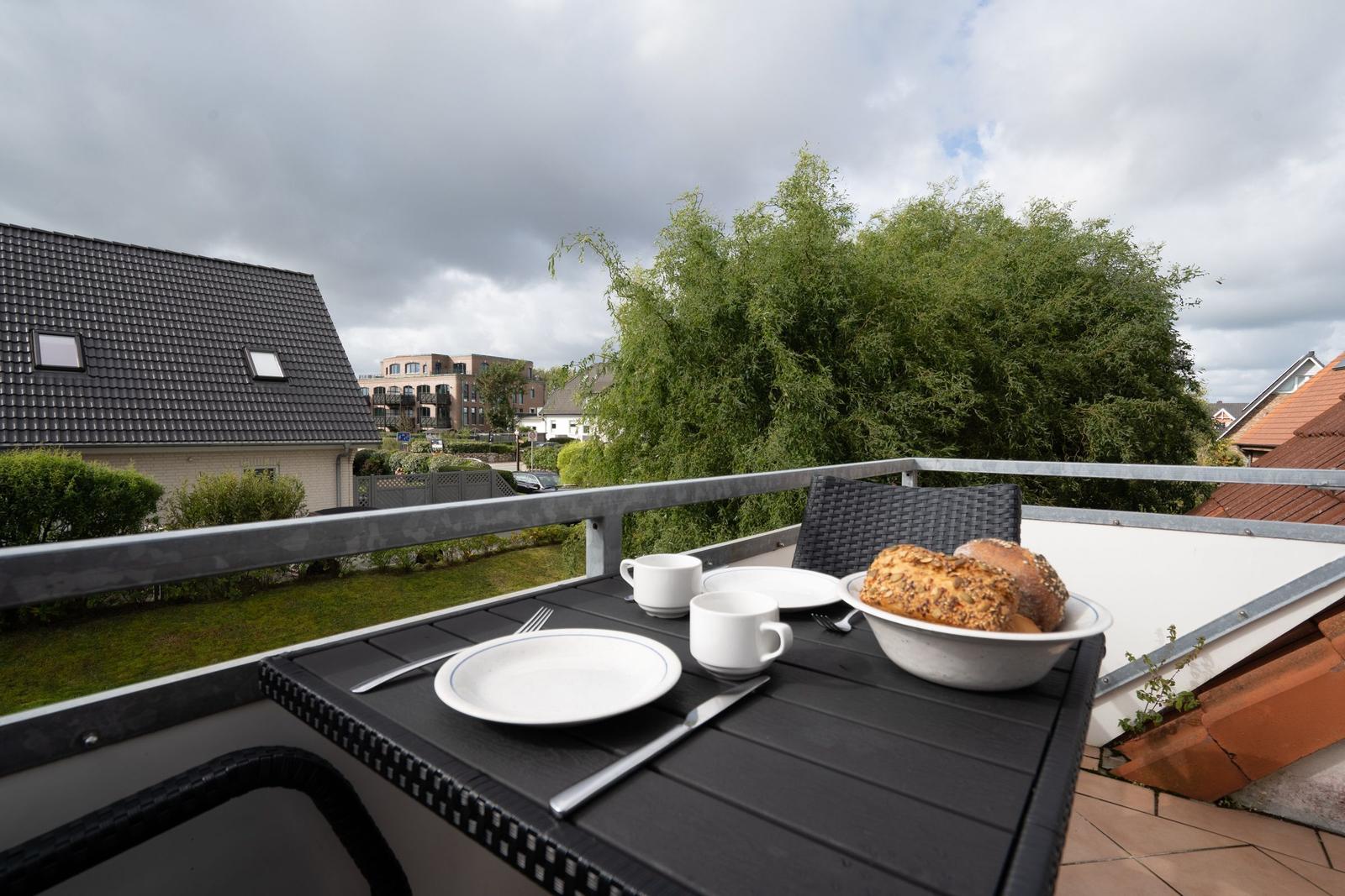 Terrasse mit Tisch, Stühlen und Frühstück. Blick auf Grün und Häuser.