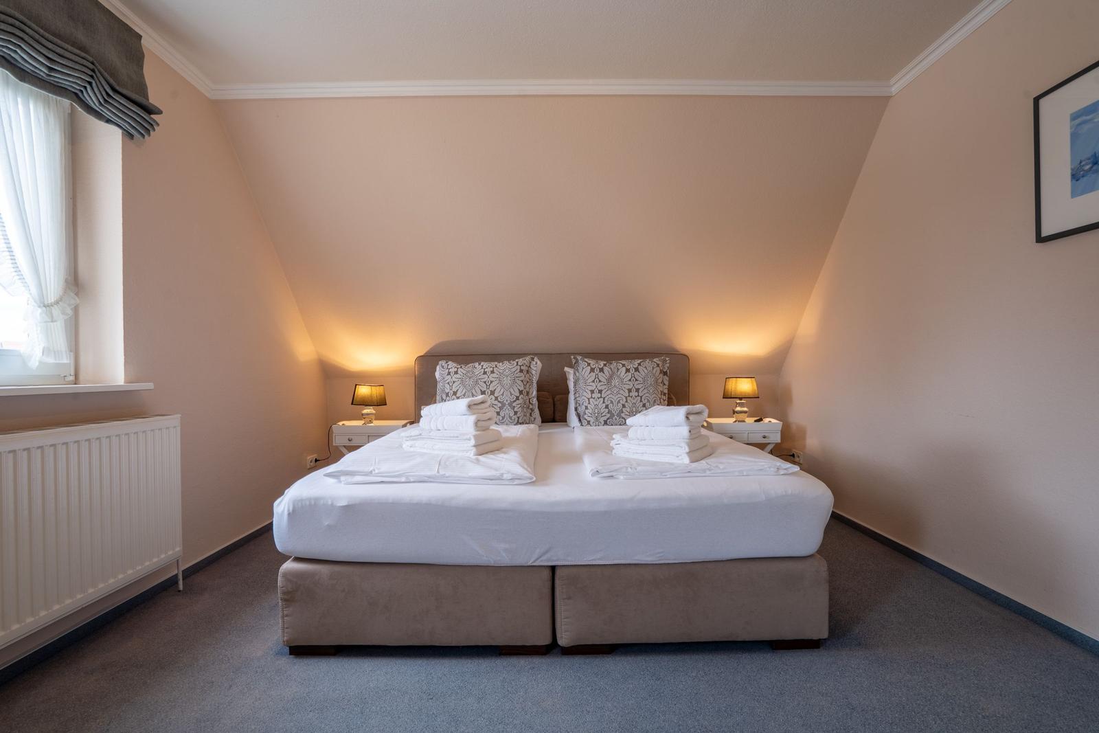 Schlafzimmer mit Doppelbett, zwei Nachttischen und Fenster.