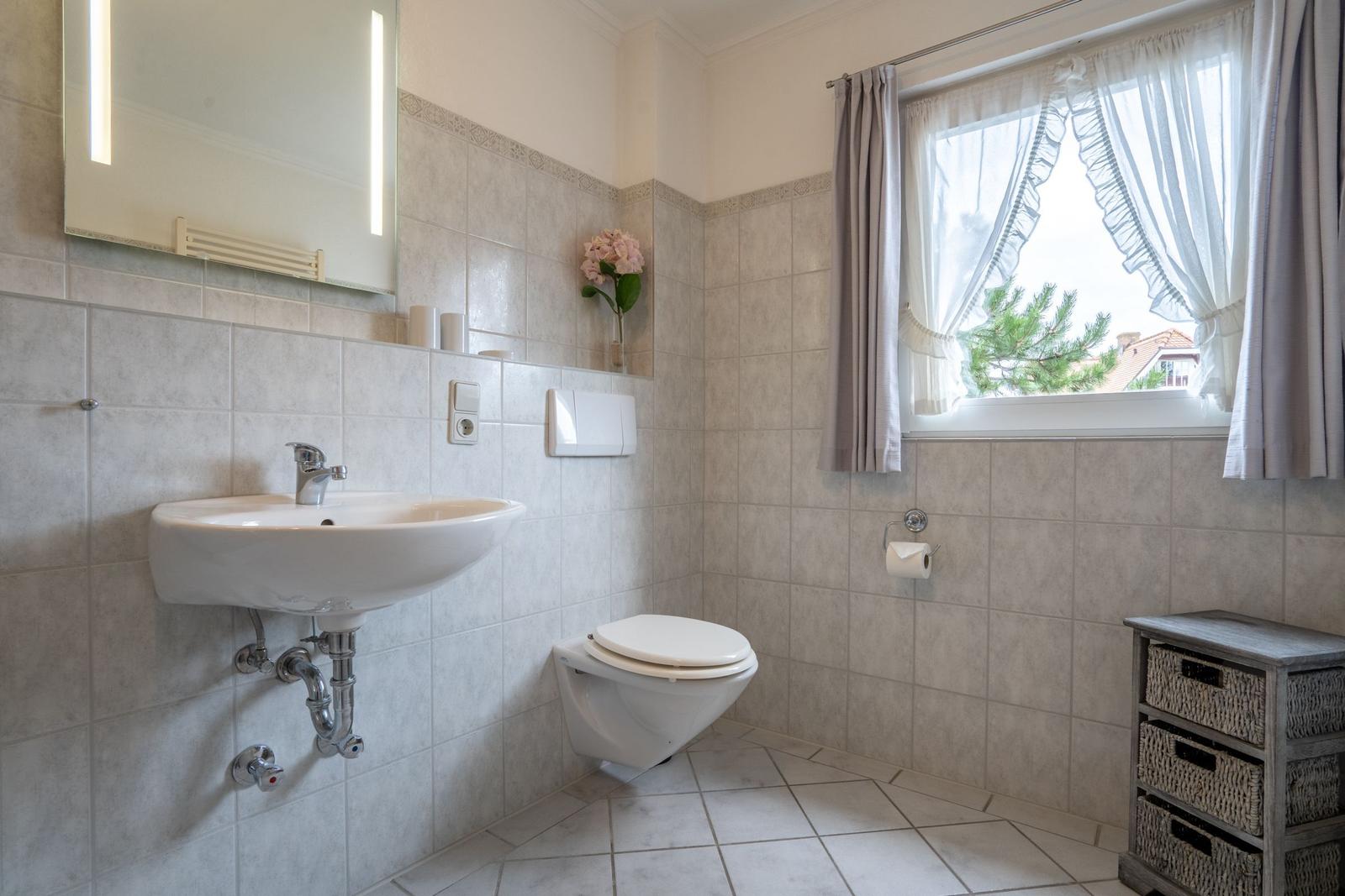 Badezimmer mit Waschbecken, Toilette und Fenster mit Vorhängen.