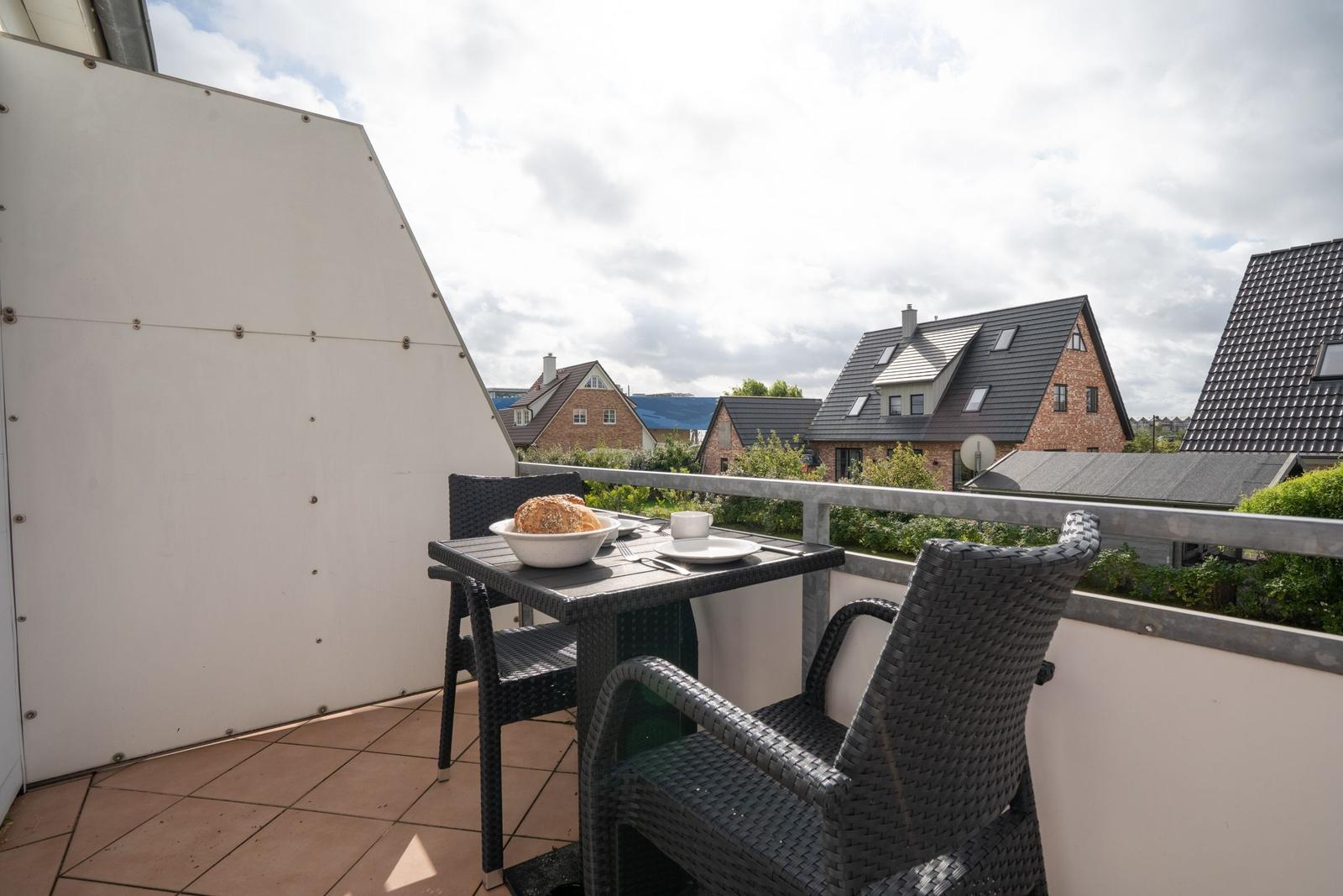 Terrasse mit Tisch und Stühlen, Blick auf Wohnhäuser und Grünflächen.