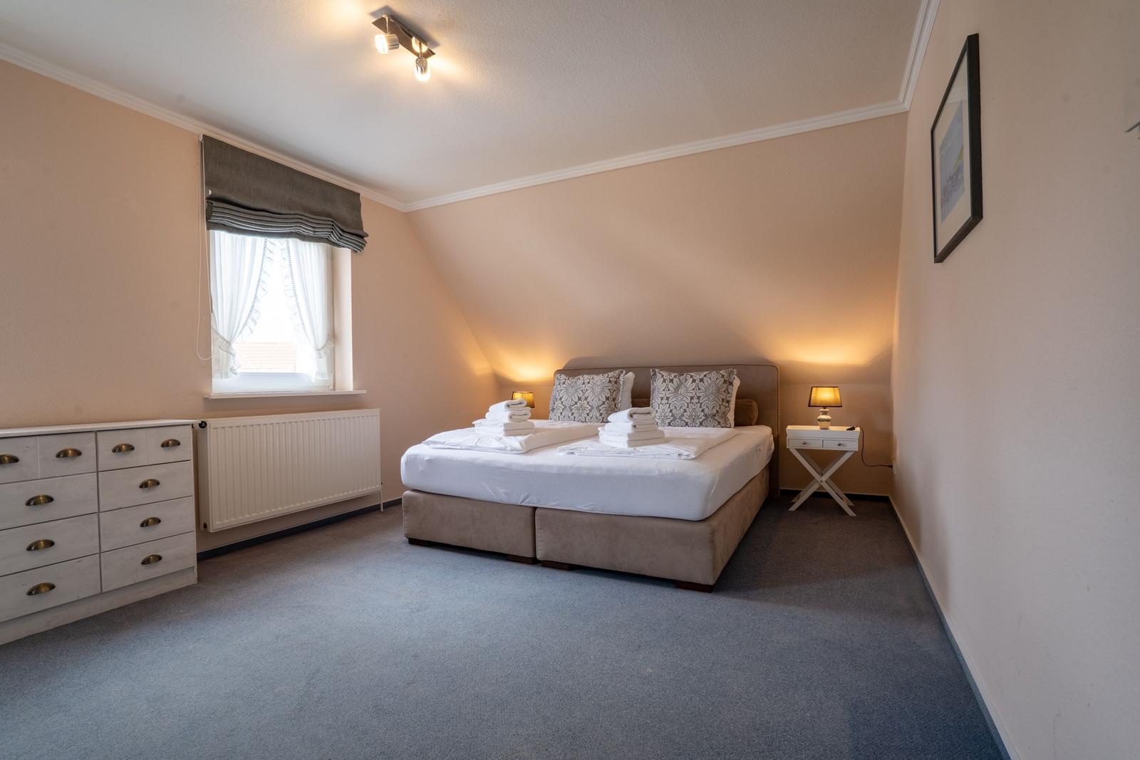 Schlafzimmer mit Bett, Nachttisch und Schrank. Fenster mit Rollladen und Heizung.