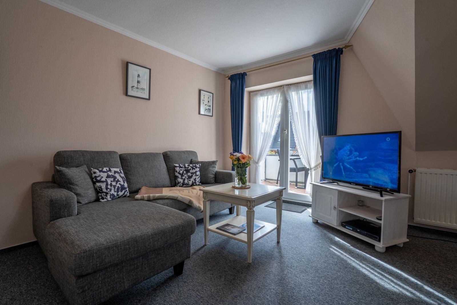 Wohnzimmer mit Sofa, TV und Balkonzugang.