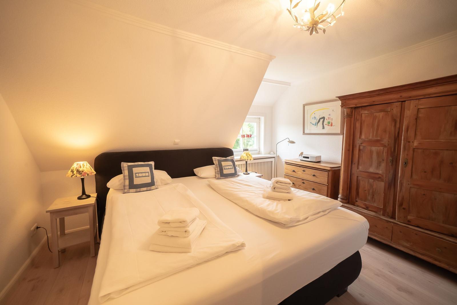 Bedroom with double bed, wooden wardrobe, and bedside table. Window with view outside.