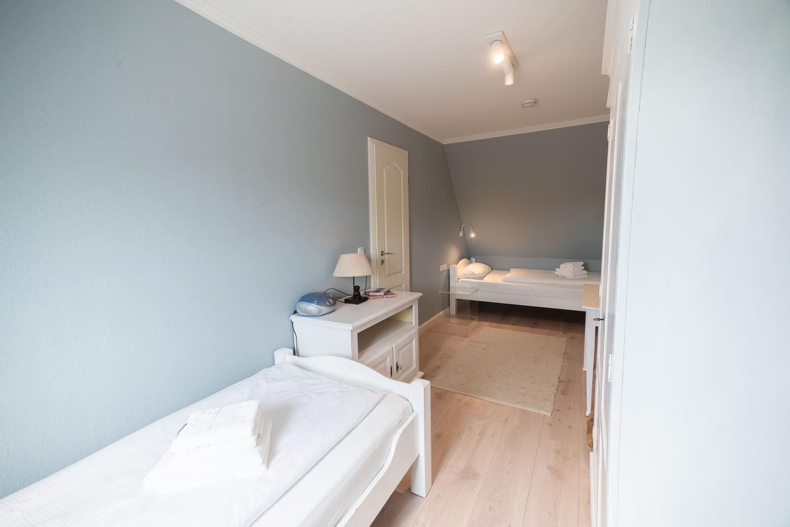 Room with two beds, wooden floor, and light walls.