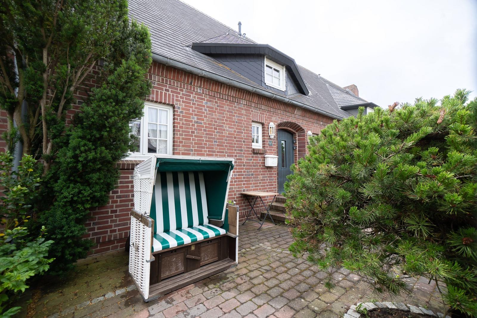 Red brick house with beach chair and green hedge in the front garden.