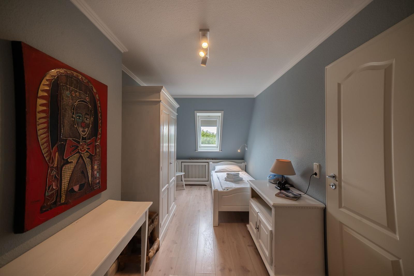 Bedroom with bed, wardrobe, and wall art. Wooden floor and window with view outside.