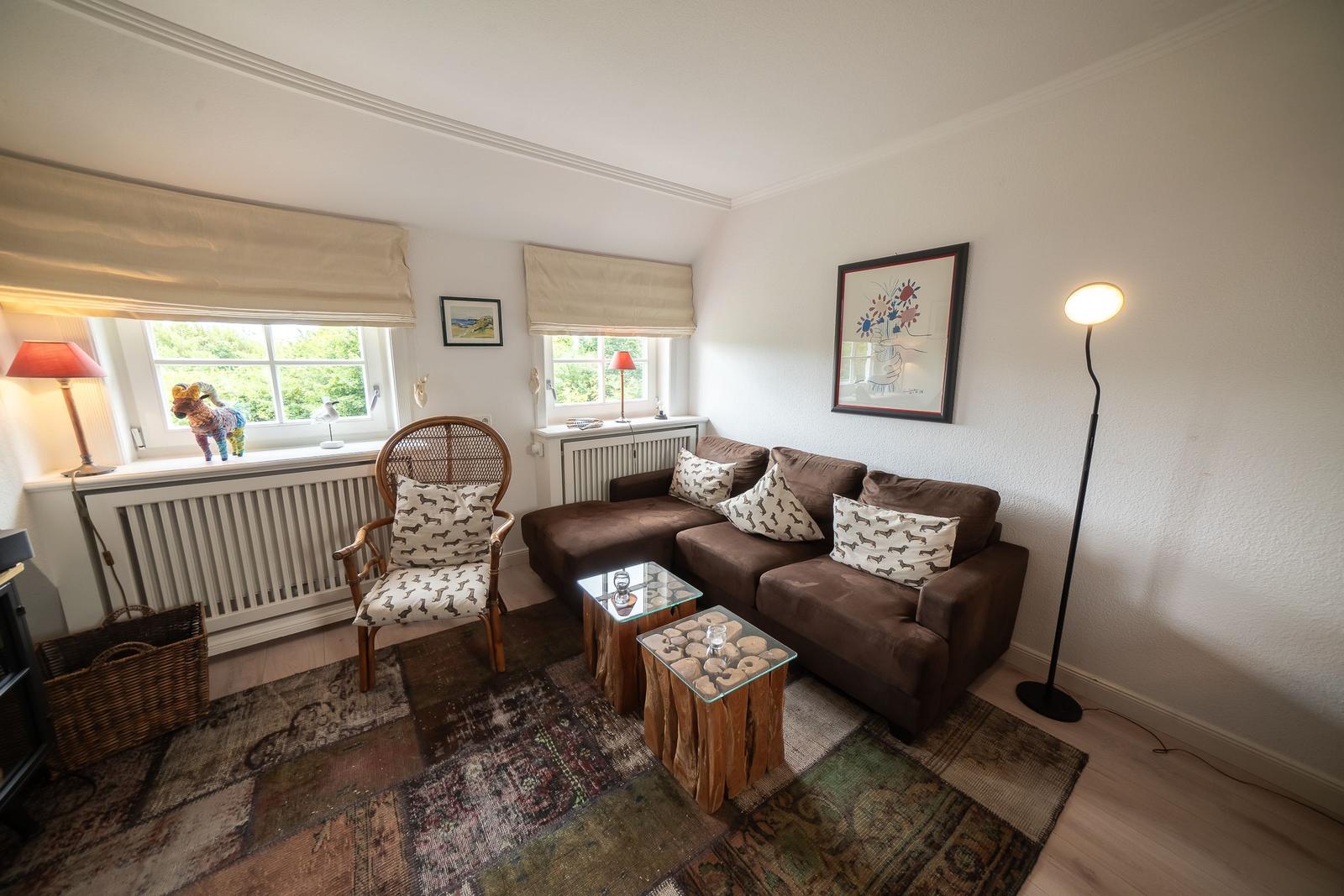 Living room with brown sofa, two tables, and two windows.