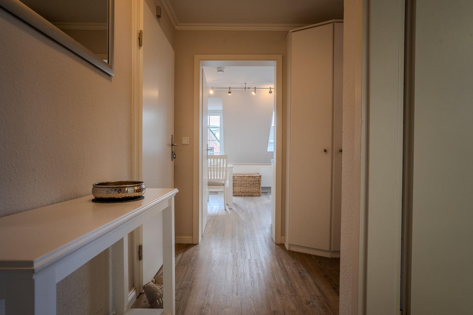 Flur mit Holzboden, Spiegelschrank und Blick in Wohnbereich mit Stuhl und Korb.