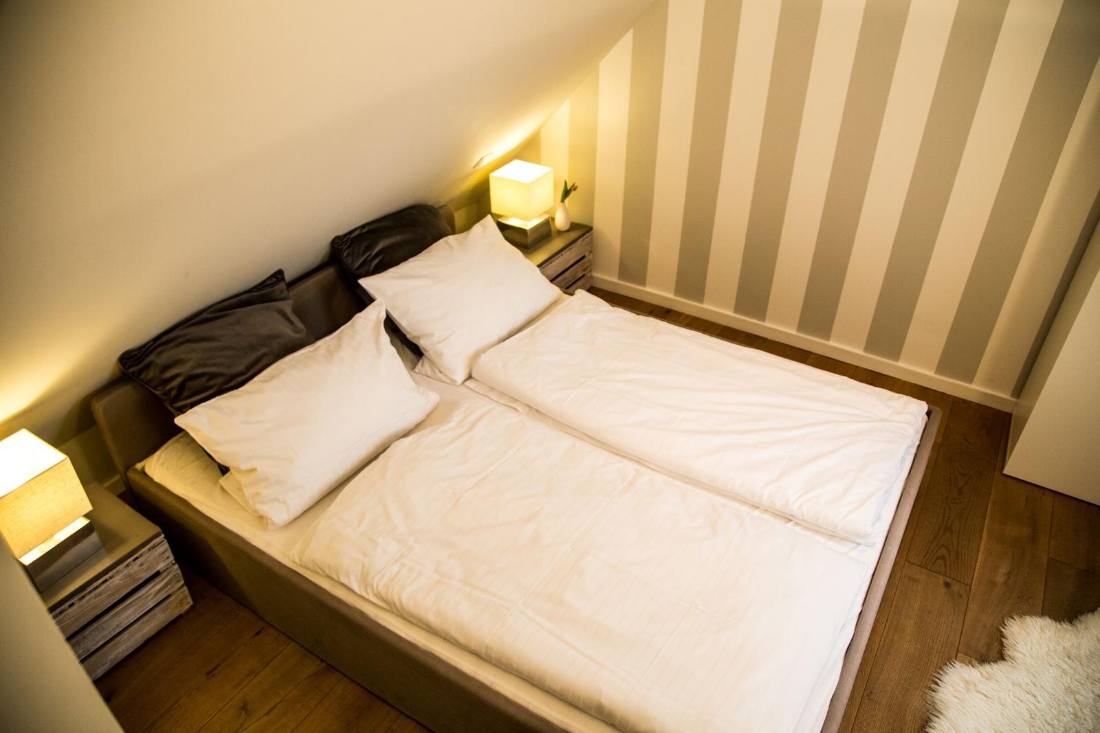 Schlafzimmer mit Doppelbett, Nachttisch und Streifenwand.