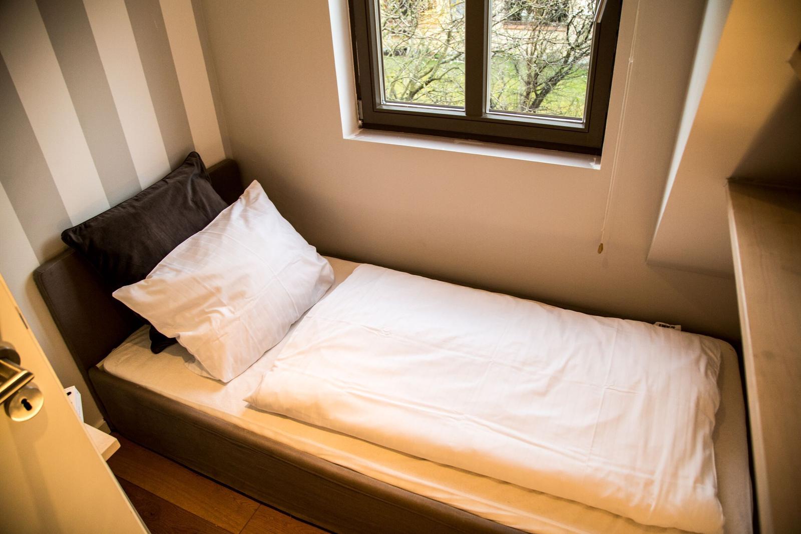 Ein Bett mit weißer Bettwäsche und einem dunklen Kissen unter einem Fenster.