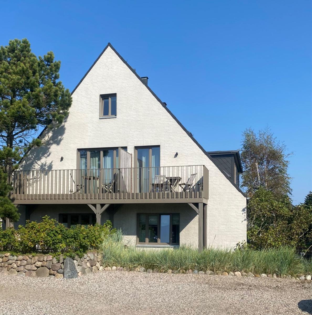 Modernes Haus mit Balkon und großen Fenstern. Umgeben von Bäumen und Gras.