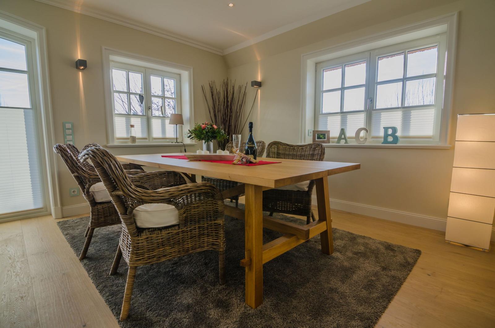 Esszimmer mit Holztisch, geflochtenen Stühlen und Fenstern mit Jalousien.