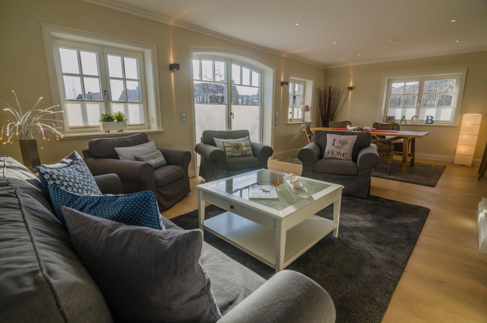 Wohnzimmer mit Sofa, Sesseln, Glas-Tisch und Holzboden.