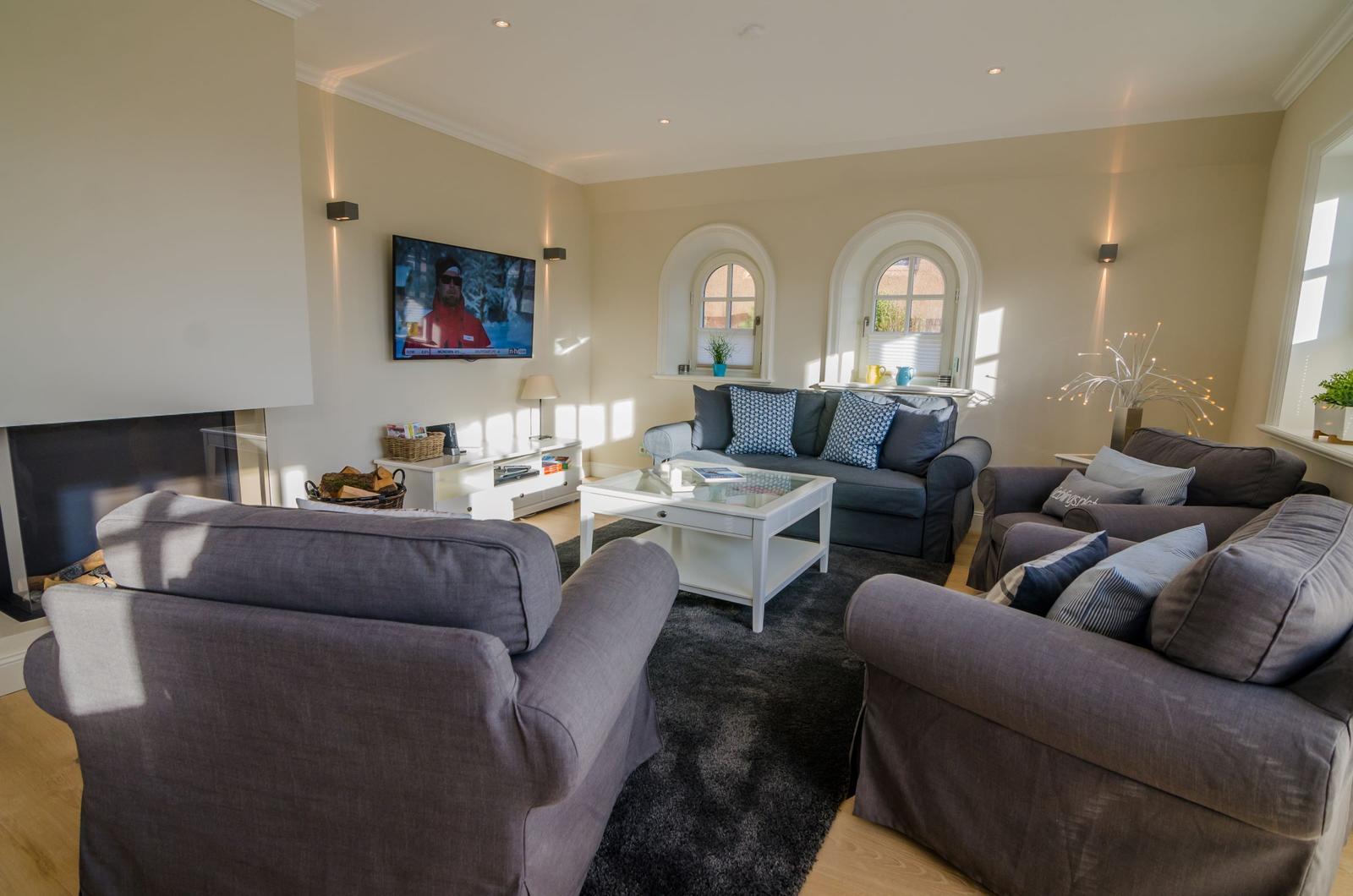Wohnzimmer mit Sofa, Sesseln, Fernseher und Kamin.