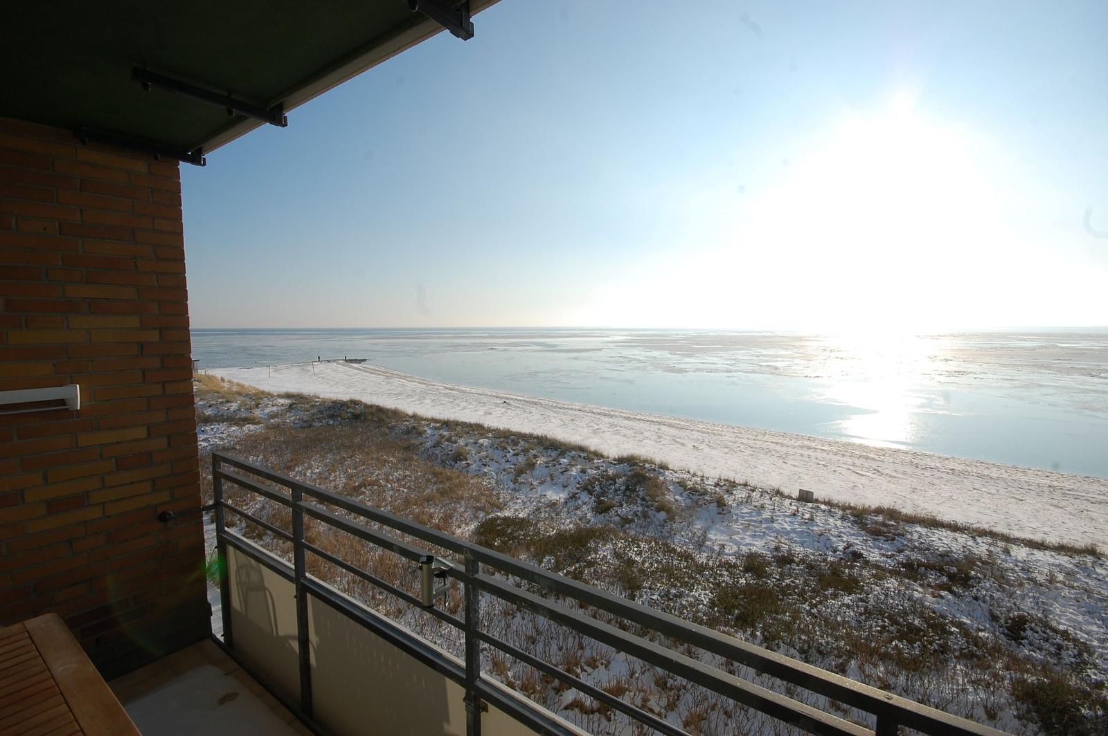 Blick von Balkon auf schneebedeckten Strand und gefrorenes Wasser.