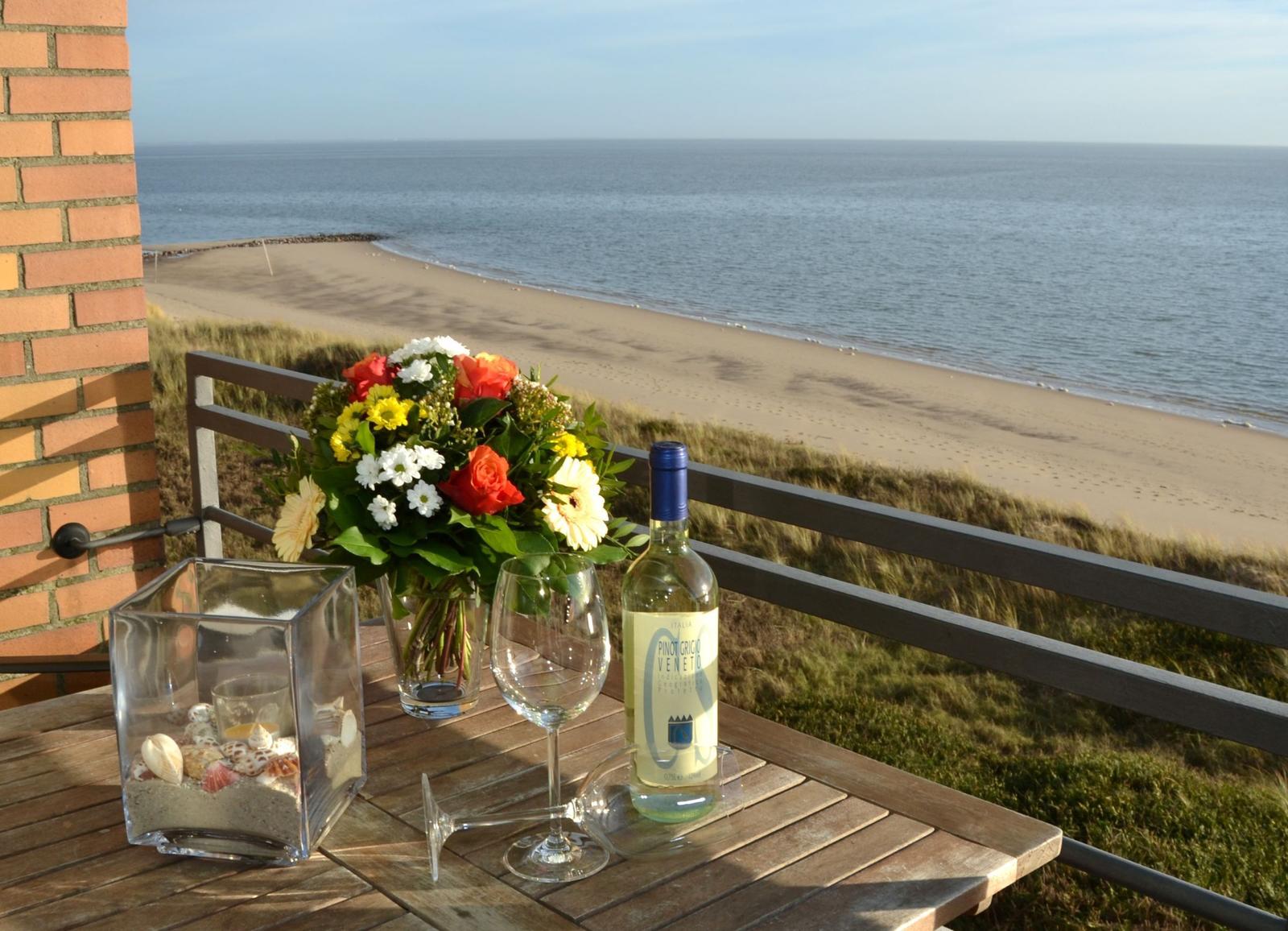 Terrasse mit Tisch, Wein und Blumen über Strand und Meer