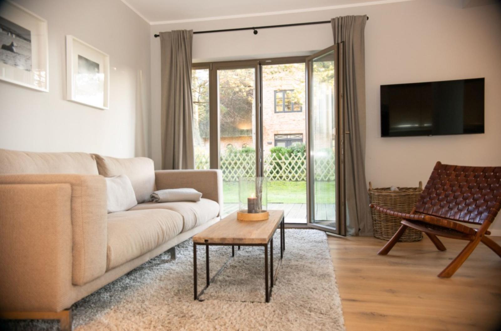 Wohnzimmer mit Sofa, Couchtisch und Fernseher. Durchgang zur Terrasse mit Blick auf Garten.
