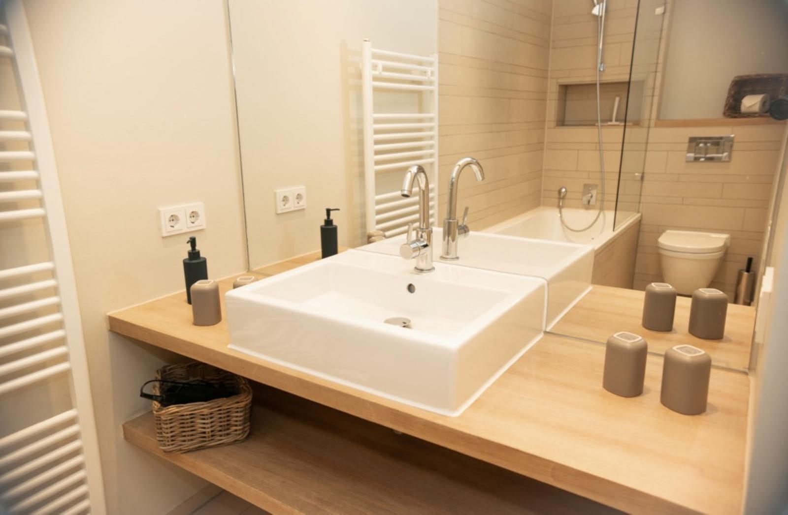 Bad mit Waschbecken, Dusche und Toilette. Holzunterlage und Spiegel.
