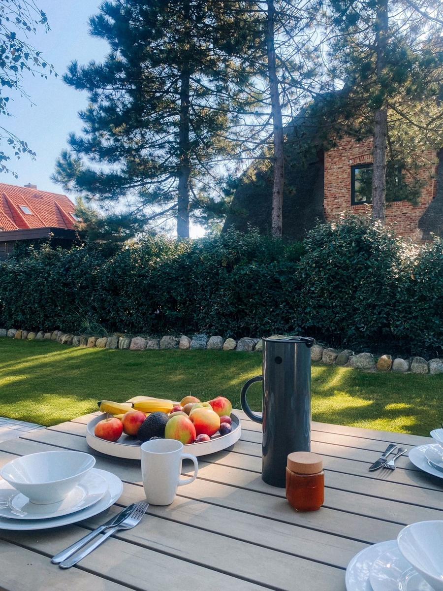 Garten-Tisch mit Obst, Tassen und Kanne im Sonnenlicht.