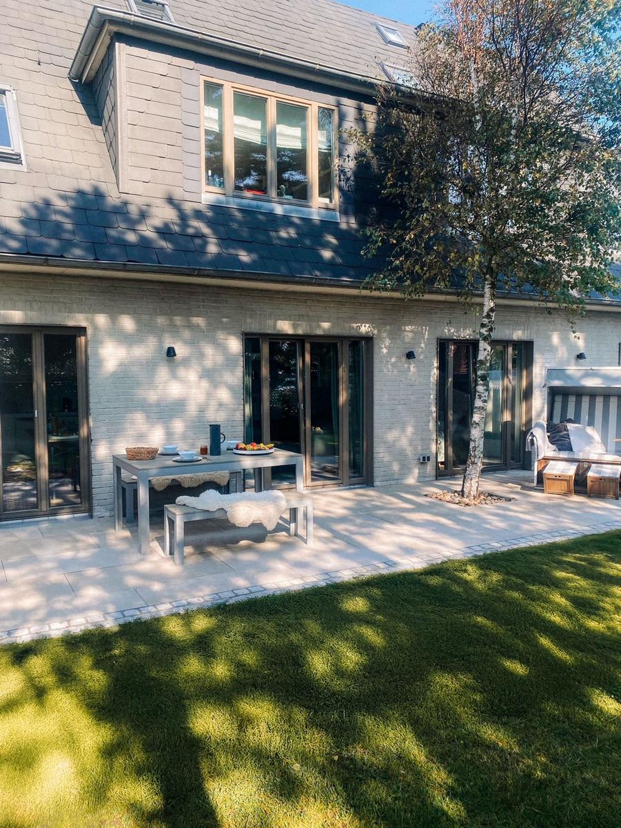 Terrasse mit Tisch, Bänken und Baum. Hinterhof mit Rasen und Glas-Türen.