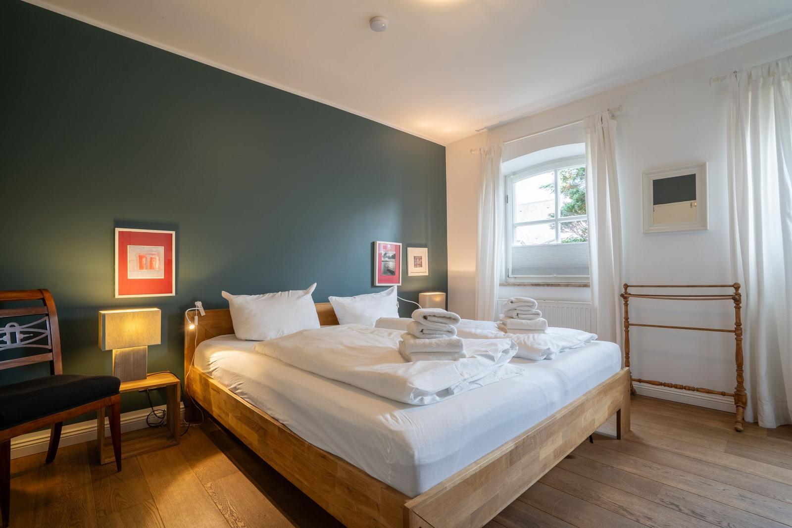 Bedroom with wooden bed, green wall, and window with white curtains.